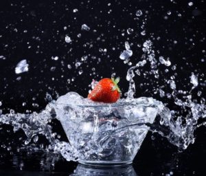 Erdbeere fällt spritzend in Schüssel mit Wasser